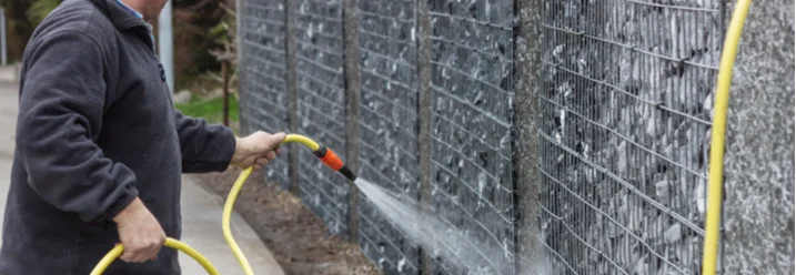 Person säubert eine Gabionenwand mit dem Gartenschlauch